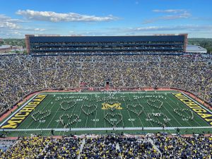 Michigan Stadium with marching band members on the field in the formation of several hearts.